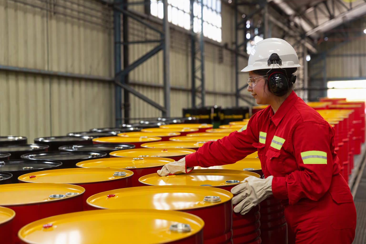 A worker wearing a hard hat, ear protection and red coveralls checks Shell lubricant drums at the plant.