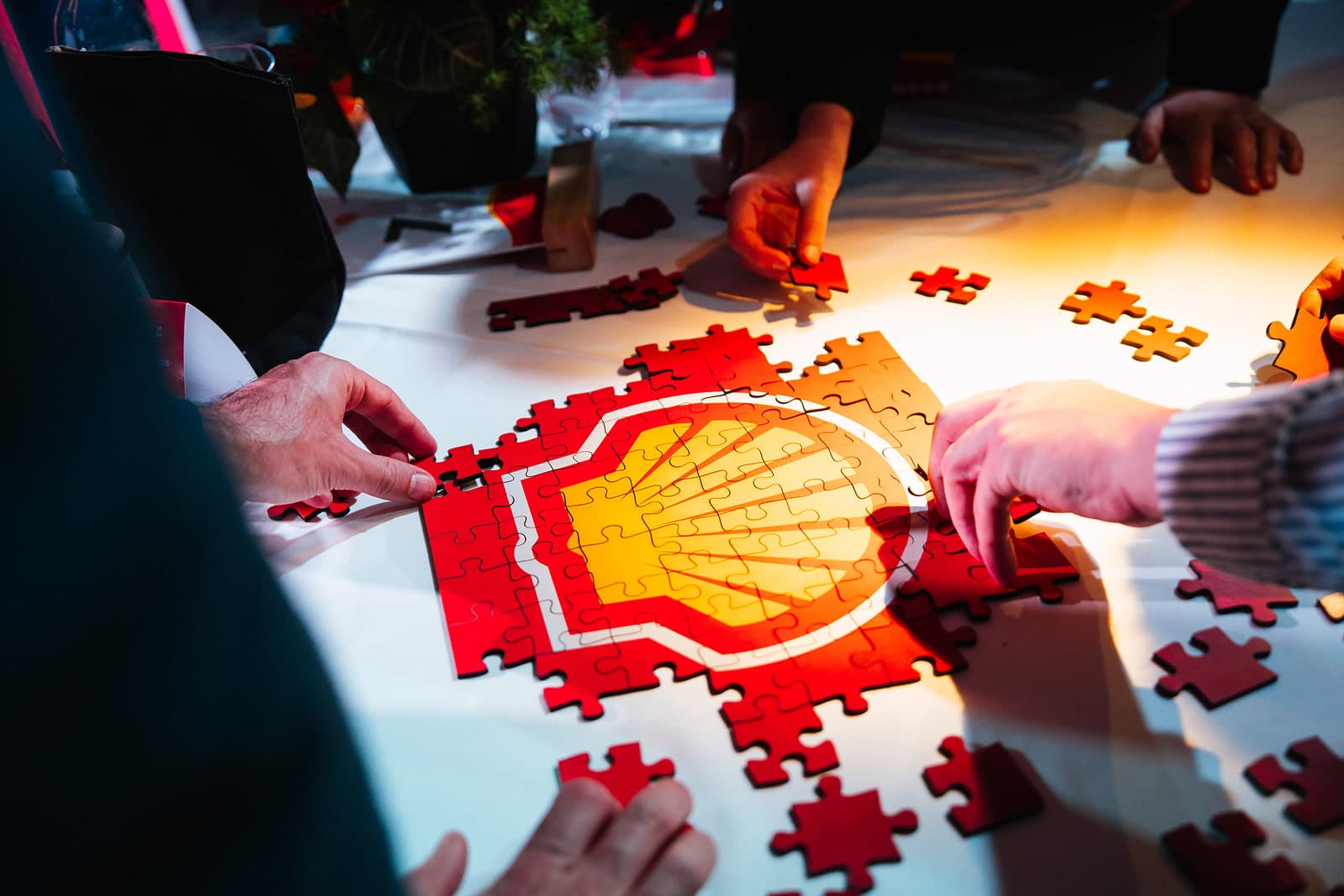 Varias manos arman sobre una mesa un rompecabezas con el logo de Shell.