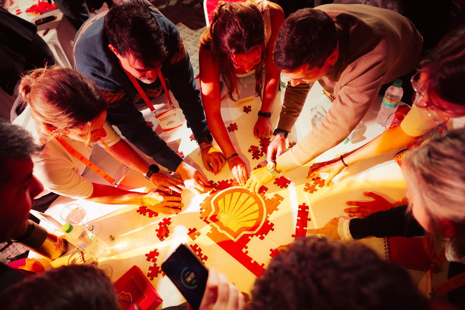 Vista desde arriba de un grupo de personas que arma sobre una mesa un rompecabezas con el logo de Shell.